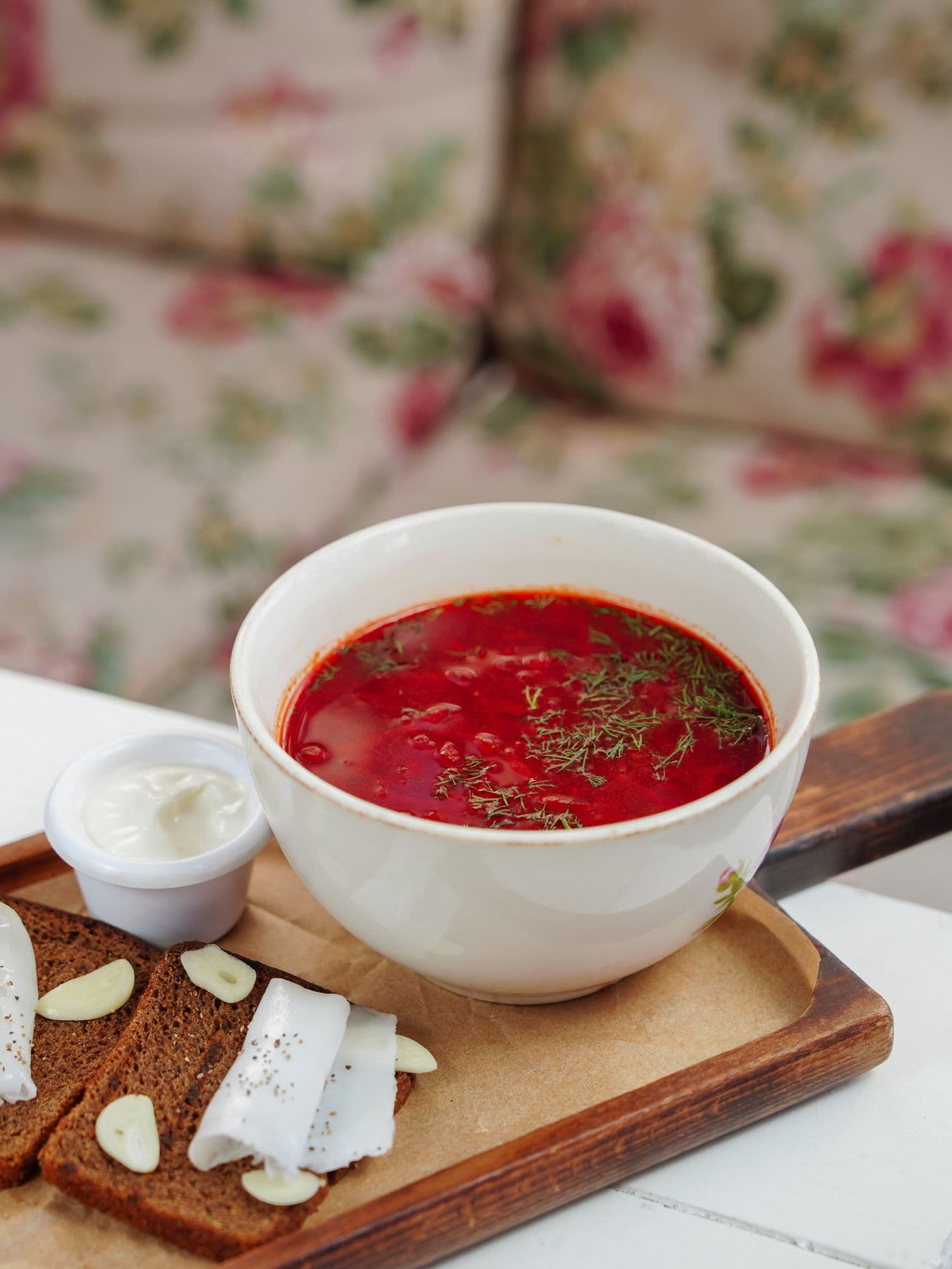 A bowl of borscht with sour cream on a flowered tablecloth